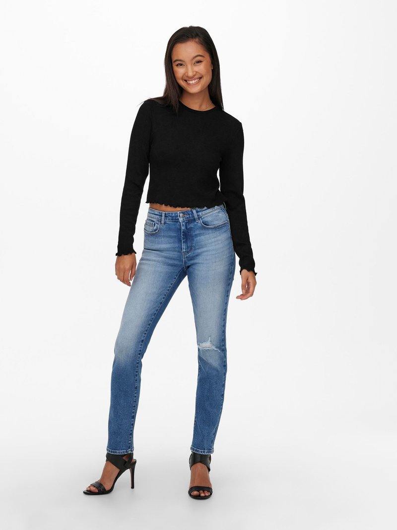 Haut cropped noir à manches longues avec un ourlet festonné, associé à un jean skinny déchiré bleu clair et des sandales à talons noirs.