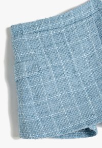 Tissu tissé de couleur bleu clair avec un motif texturé en damier. Présente des accents blancs et argentés, des bords effilochés et une finition douce.
