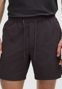 Tummanharmaat shortsit, jotka on valmistettu kevyestä kankaasta. Niissä on joustava vyötärö nauhalla, sivutaskut ja teksturoitu muotoilu.