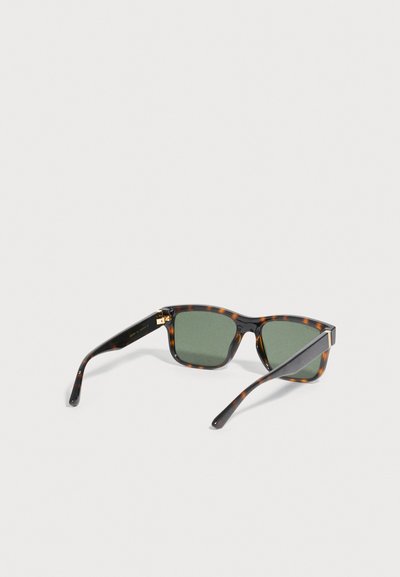 Ορθογώνια γυαλιά ηλίου με σχέδιο χελώνας, σκοτεινούς πράσινους φακούς και ελαφρώς κυρτά μπράτσα που ακουμπούν σε φωτεινή επιφάνεια.