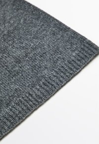 Graues gestricktes Gewebe mit einer strukturierten Oberfläche und geripptem Rand; weicher Eindruck, teilweise gefaltet, vor einem weißen Hintergrund.