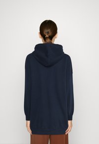 Sudadera con capucha de color azul marino, de mangas largas, corte relajado y puños acanalados, fabricada en un tejido suave. La vista desde la parte posterior muestra un diseño minimalista.