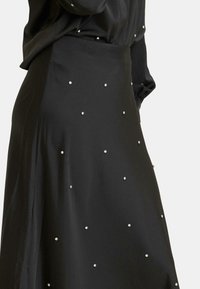 Falda de satén negra con tachuelas de plata dispersas, que presenta una textura suave y un diseño fluido, diseñada para una silueta elegante.