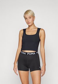 Crni crop top s kvadratnim izrezom, uparen s crnim šortsevima koji imaju struk s bijelim Puma logotipom, izrađen od rastezljivog, atletskog materijala.