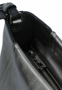 Innenseite einer schwarzen Lederhandtasche mit einem Reißverschlussfach, glatter Textur und metallischen Beschlägen. Schattierungen heben die Designdetails hervor.
