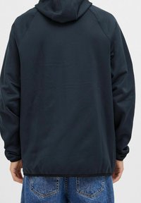 Laivastonsininen huppari, jossa on sileä pinta ja rento istuvuus. Hupparissa on raglan-hihat ja yksinkertainen muotoilu, jota on yhdistetty vaaleisiin farkkuihin.