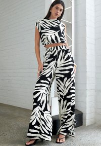 Melnbaltā lapu raksta divdaļīgā apģērba komplekts, kas ir veidots no īsā topa un platajiem biksēm ar elastīgu jostasvietu un sānu saitēm.