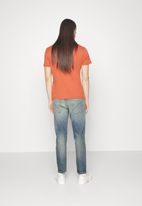 Oranges T-Shirt mit kurzen Ärmeln, kombiniert mit hellblauen Jeans im geraden Schnitt und subtilen Verblassungen, getragen mit weißen Schuhen.