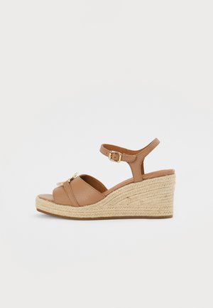 Brown leather wedge sandals with a woven jute base. Features an ankle strap with a metal buckle and two crossed front straps.