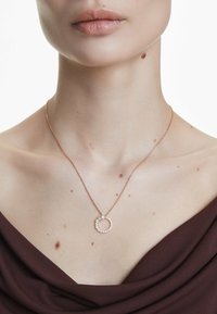 Rose gold halskæde med en cirkulær vedhæng, der har en perle og en cirkulær opstilling af klare sten. Glat, delikat kædedesign.