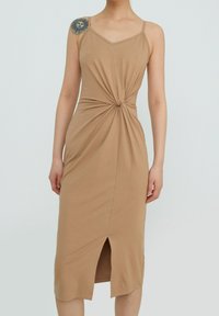 Robe midi beige avec fines bretelles, détail torsadé devant et fente frontale. Fabriquée en tissu doux et extensible avec une texture lisse.