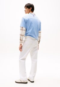 Light blue short-sleeve t-shirt layered over a plaid long-sleeve shirt, paired with white jeans and cream sneakers. Simple and modern design.