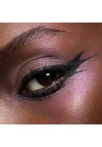 Gros plan sur un œil avec un eyeliner noir en forme d'ailes, un fard à paupières rose irisé subtil et une iris brun foncé avec de longs cils sur une peau lisse.