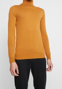 Jersey de cuello alto color mostaza en tejido de punto suave y acanalado. Diseño ajustado con mangas largas y puños rematados. Acabado sencillo y sin costuras.