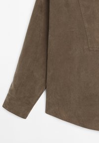 Chemise en suede marron à manches longues, avec un col pointu et un ourlet légèrement arrondi. Le matériau a une texture douce avec peu de détails.