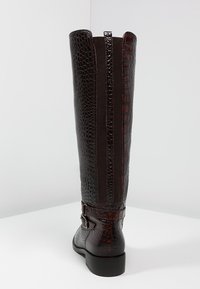 Botte haute jusqu'au genou en cuir marron effet croco avec panneaux latéraux élastiques, accent de boucle à la cheville et talon bloc bas. Détails de surface texturée.