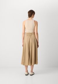 Débardeur beige associé à une jupe beige fluide arrivant aux genoux avec une taille élastique. Chaussures blanches avec un petit talon noir.