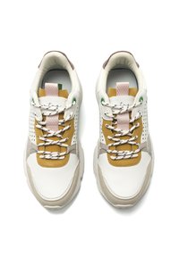Les baskets présentent un mélange de matériaux blancs, beiges et moutarde, avec des accents perforés, des lacets à motifs et des œillets verts pour plus de détails.