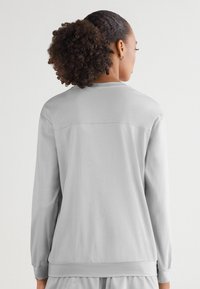 Ljusgrå sweatshirt med långa ärmar, rundad halsringning och ribbade muddar. Slät textur; minimala sömmar och detaljer på baksidan.
