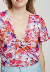 Haut à imprimé floral avec un décolleté en V profond, un détail froncé au centre, des manches courtes et un tissu léger et aéré dans des couleurs vives.