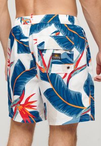 Bañadores para hombre con un estampado floral en azul, verde y naranja sobre un fondo blanco. Cintura elástica con un bolsillo en la parte trasera.