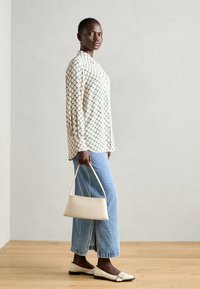 Long-sleeve cream shirt with green diamond pattern, paired with light blue wide-leg jeans and white flats. Accessory: small white handbag.