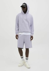 Ljuslila huvtröja med känguruficka, matchad med shorts i samma färg. Vita sneakers och randiga strumpor fulländar outfiten. Svart keps på huvudet.