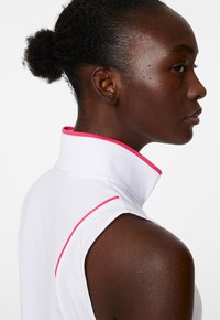 Vit ärmlös topp med hög krage och rosa detaljer. Slät textur, atletisk passform och en ren design.