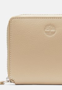 Portafoglio in pelle beige con superficie texturizzata, dotato di chiusura a zip e logo impresso. Include cuciture in contrasto e dettagli in metallo.