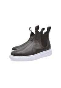 Botas de tobillo de cuero marrón con laterales elásticos, punta redondeada y suela de goma blanca. Presentan tiradores para facilitar el uso. Textura suave.
