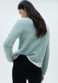 Maglione azzurro chiaro, con texture e maniche lunghe. Indossato sopra una camicia bianca, abbinato a leggings neri. Presenta un collo rotondo e una vestibilità comoda.