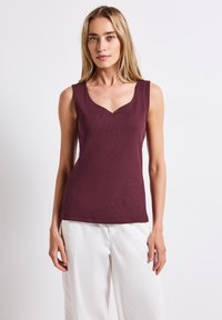 Burgunderfarbene ärmellose Bluse mit V-Ausschnitt, gerippter Textur und taillierter Silhouette, kombiniert mit weißen weitem Hosen.
