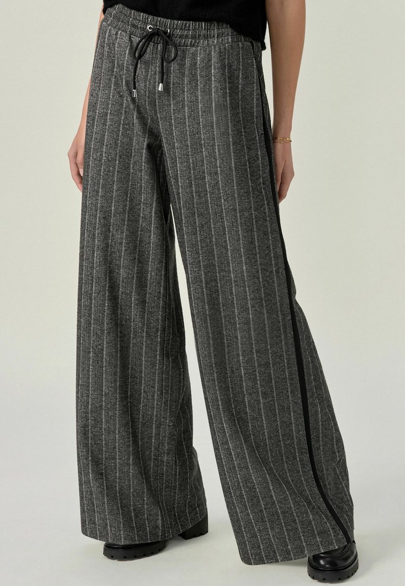 Graue gestreifte High-Waist-Hosen mit elastischem Bund, Kordelzug und seitlichem Akzentstreifen. Hergestellt aus weichem Material mit strukturiertem Finish.