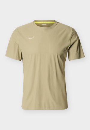 T-shirt de sport beige clair à manches courtes avec col rond et petit logo blanc HOKA sur la poitrine gauche, présenté sur un fond uni.