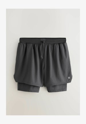 Graue Sportshorts mit einem mehrlagigen Design, ausgestattet mit einem elastischen Bund, verstellbarem Kordelzug und Innenfutter. Glatte Textur durchgehend.
