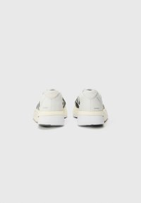 White and black athletic shoes with a textured mesh upper, a padded collar, and a rubber sole; minimalist design with subtle branding.