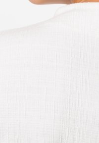 Tessuto bianco testurizzato con un sottile motivo intrecciato, caratterizzato da una sensazione morbida e leggera. Il design mostra un collo rotondo dalla vista posteriore.