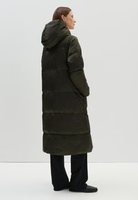 Lange donsjas in donkerolijfgroen met een capuchon, voorzien van een gestikt ontwerp, zachte glans en geribde manchetten. Lichtgewicht en enkel-lang.