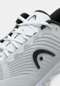 Suur lähivõte hallist spordijalatsist valgete paeltega, must logo külgedel ja must polsterdatud sisu.