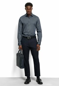 Dunkelblauses gemustertes Hemd mit Knöpfen, schwarzer Gürtel, marineblaue Hose und schwarze Schuhe. Trägt eine dunkelblaue Lederaktentasche.