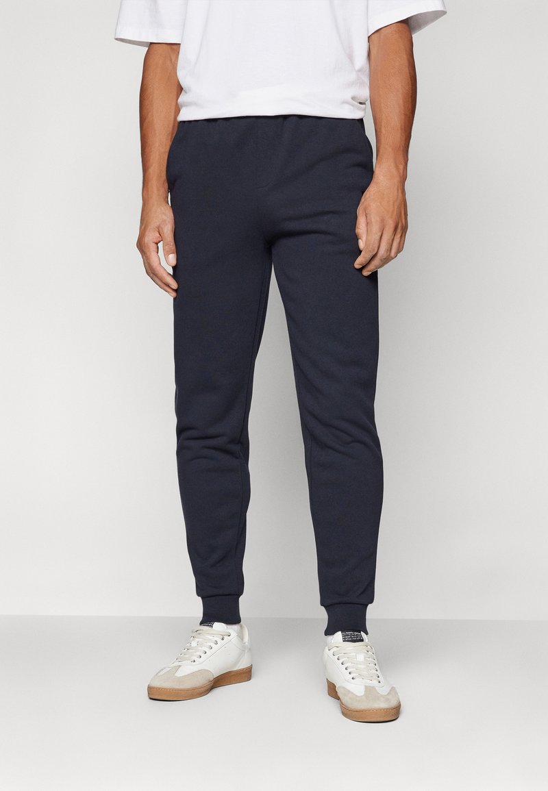 Joggers in cotone blu navy con un design aderente, polsini a coste e una vita elasticizzata. Abbinati a sneakers bianche con dettagli beige.