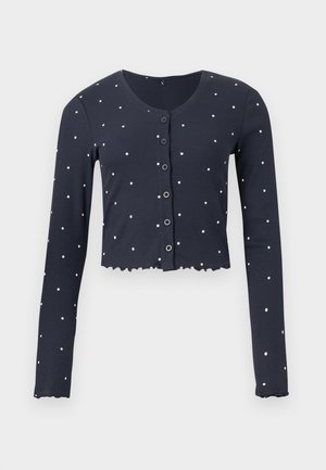 Κοντή ζακέτα σε ναυτικό μπλε με λευκές πουά τελείες, μακριά μανίκια, κουμπιά μπροστά, στρογγυλή λαιμόκοψη και βολάν στα τελειώματα και στα μανίκια.