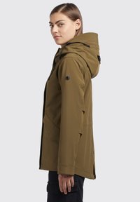 Giacca impermeabile verde oliva con cappuccio, dotata di tasche con zip, lacci regolabili e un design elegante e aerodinamico.