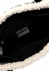 Black bag interior with a fluffy white lining, textured zip closure, and a leather label. Smooth fabric with a deep, spacious design.