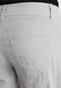 Jasnoszare lniane spodenki z tylną kieszenią o prostym górnym brzegu i subtelną fakturą, uzupełnione białym przeszyciem i prostym wzornictwem.