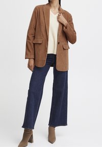 Brun manchesterblazer med två framfickor, över en krämfärgad stickad tröja, matchad med mörka vida jeans och tanfärgade klackboots.