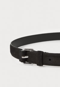 Cinturón de ante negro con un diseño suave y redondeado, herrajes en tono plateado y un lazo de cuero cosido para un ajuste seguro.