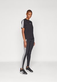 Maglietta sportiva nera a maniche corte con strisce bianche, abbinata a leggings neri con strisce laterali bianche e scarpe da corsa nere.
