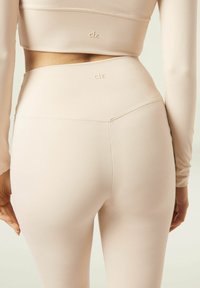 Ensemble de vêtements de sport rose clair comprenant un haut ajusté à manches longues et un legging taille haute, fabriqué dans un tissu lisse et extensible avec des logos discrets.