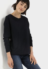 Zwart langslievend shirt met een ronde halslijn, gemaakt van zachte stof. Gecombineerd met donkerblauwe jeans, is de pasvorm ontspannen. Eenvoudig ontwerp, geen patronen.